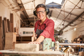 Eine junge Frau mit Hörschutz arbeitet in einer Holzwerkstatt