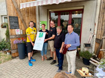 Minister Sven Schulze übergibt das Hofschild "Kulinarischer Stern" an die Inhaber der Schafmilchkäserei JAARE in Lindau.