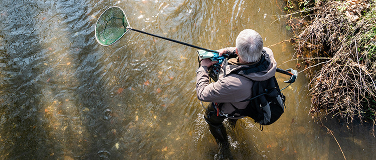 Mann mit Fischernetz im Bach stehend